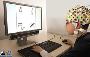 A participant in an EEG research study wears a cap covered in electrodes. The participant looks at a computer screen with four line drawings on it. They have one hand on the keyboard, and one hand on the mouse.